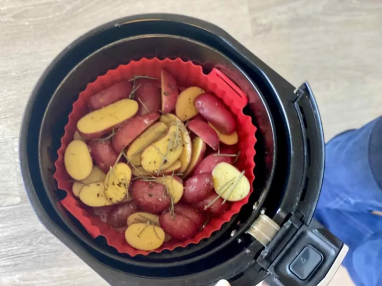Krájené brambory s bylinkami v košíku horkovzdušné fritézy.