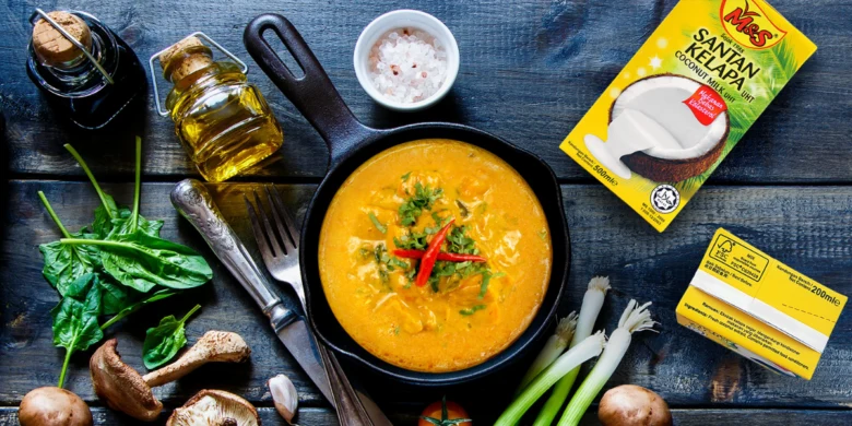 Kokosové mléko v kari s čerstvými zeleninovými ingrediencemi na dřevěném stole.