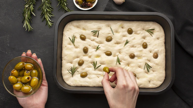 Ruce přidávají zelené olivy na surovou těsto pro domácí italskou focaccii.