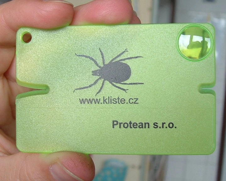 Zelený nástroj na vyndání klíště ve tvaru klíšte držený v ruce.