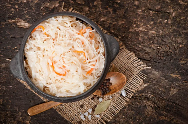 Kysané zelí s mrkví v hrnci na dřevěném povrchu