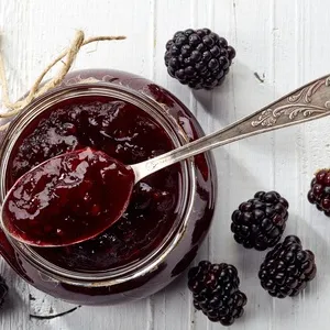 Sklenice ostružinové marmelády bez zrníček s lžící a čerstvými plody.