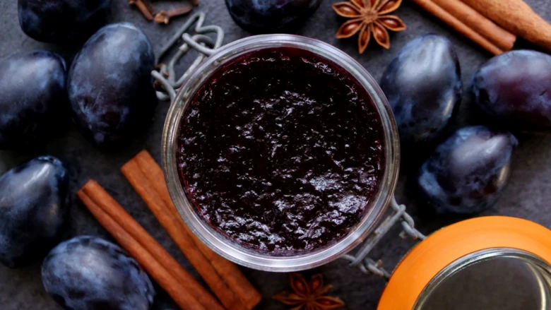 Sklenice domácí švestkové marmelády s čerstvými švestkami a kořením.