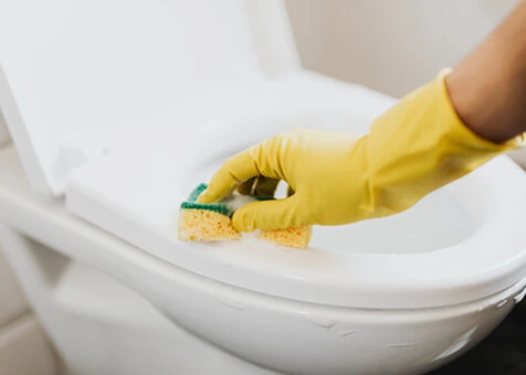 Ruka v žluté rukavici čistí WC špongiou.