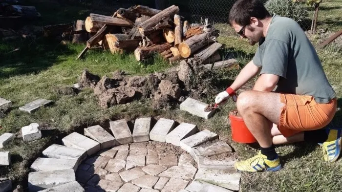 Muž staví kamenné ohniště na trávníku s dřevo.