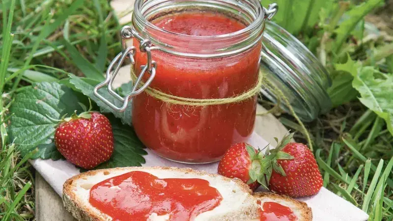 Sklenice jahodového džemu s čerstvými jahodami na chlebu.