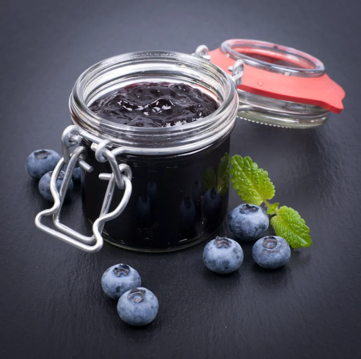 Blueberry jam jar with fresh berries and mint leaves on dark