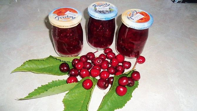 Tři sklenice domácí višňové marmelády s čerstvými višněmi.