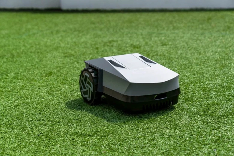 Moderní robotická sekačka na trávu stojí na umělé trávě.