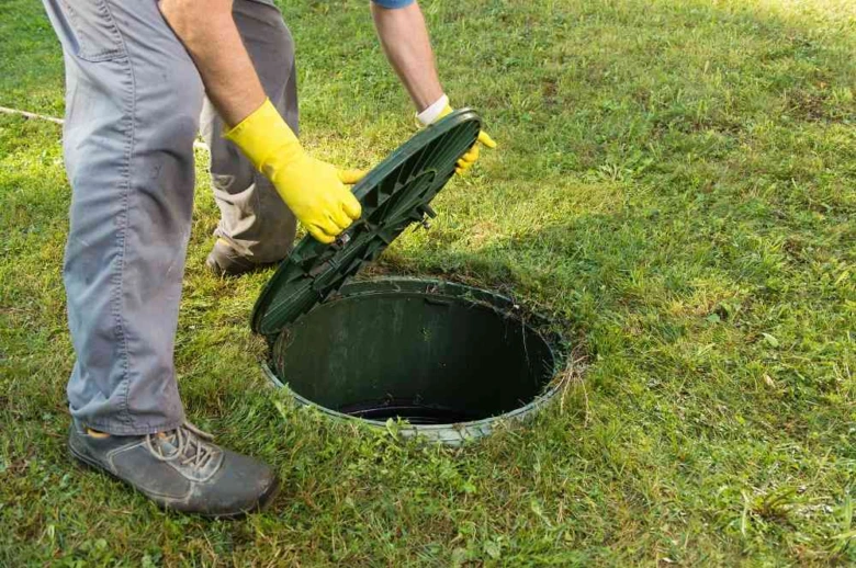 Pracovník kontroluje septik na zahradě po otevření poklopu.