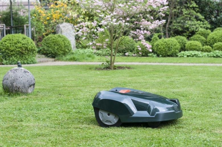 Zelená robotická sekačka na trávu v zahradě.