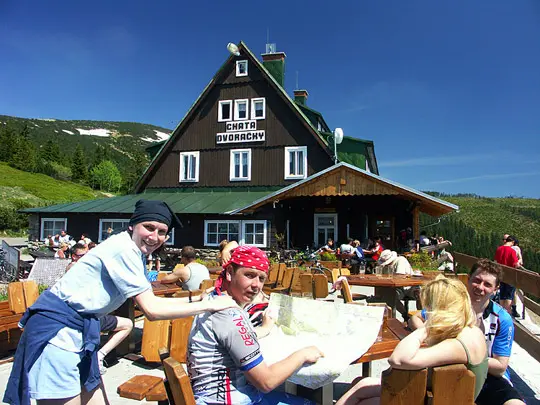 Turisté sedí u chaty Dvoráčka s horami na pozadí.