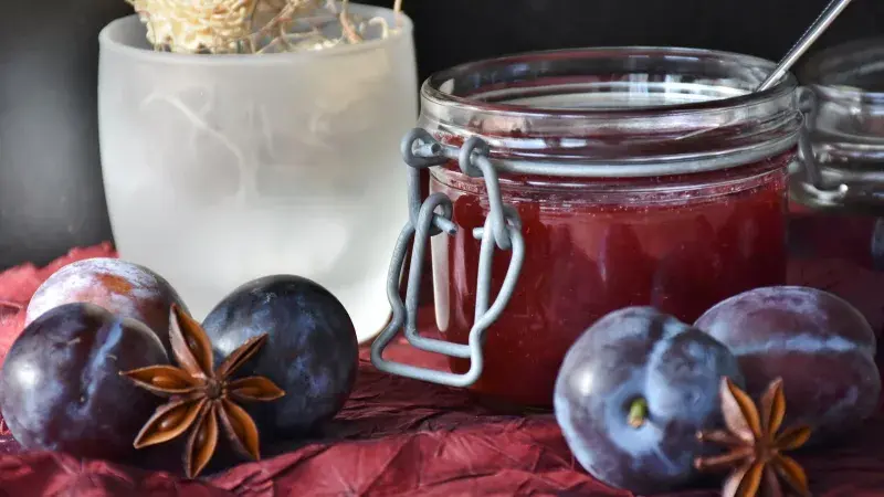 Sklenice domácí švestkové marmelády s čerstvými švestkami.