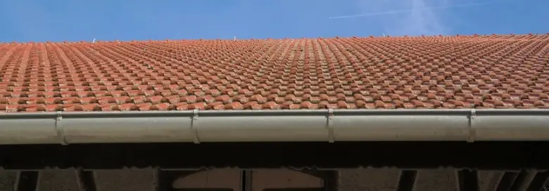 Bílý okap na červené taškové střeše pod modrou oblohou.