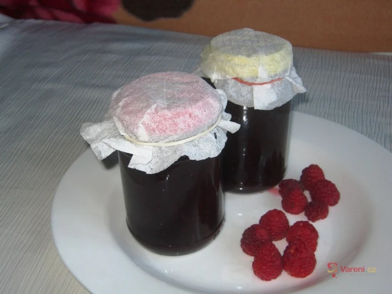 Dva sklenice malinové marmelády s čerstvými bobulemi na talíři.