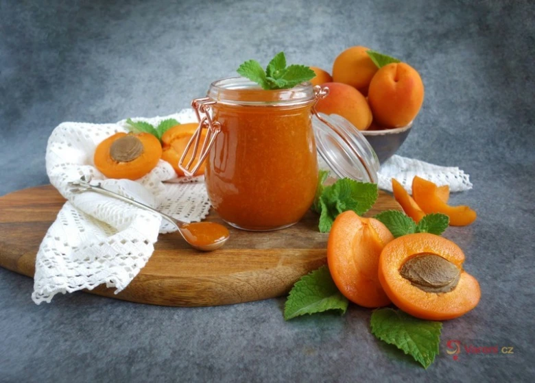 Sklenice meruňkové marmelády s čerstvými meruňkami na dřevěném talíři.