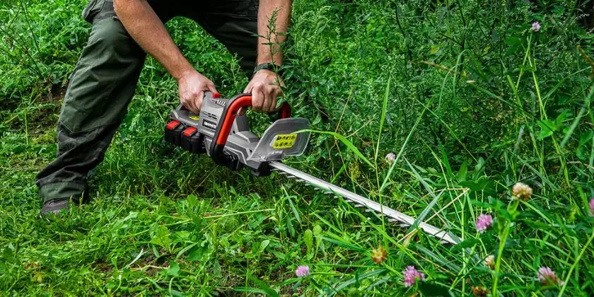 Muž řezá vysokou trávu elektrickými nůžkami na živý plot venku.