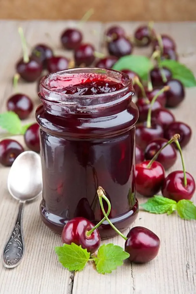 Sklenice domácí višňové marmelády s čerstvými višněmi.
