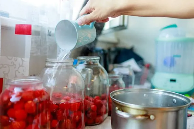 Lid nalévá sirup do sklenice s jahodami na domácí zavařování.