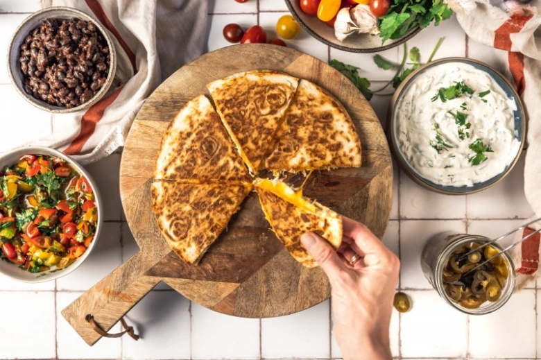 Ruce drží kousky zlatavé quesadilly s mexickými přílohami.