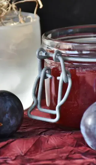 Sklenice domácí švestkové marmelády s čerstvými švestkami.
