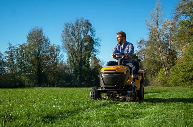 Muž řídí žlutý zahradní traktor na trávníku.