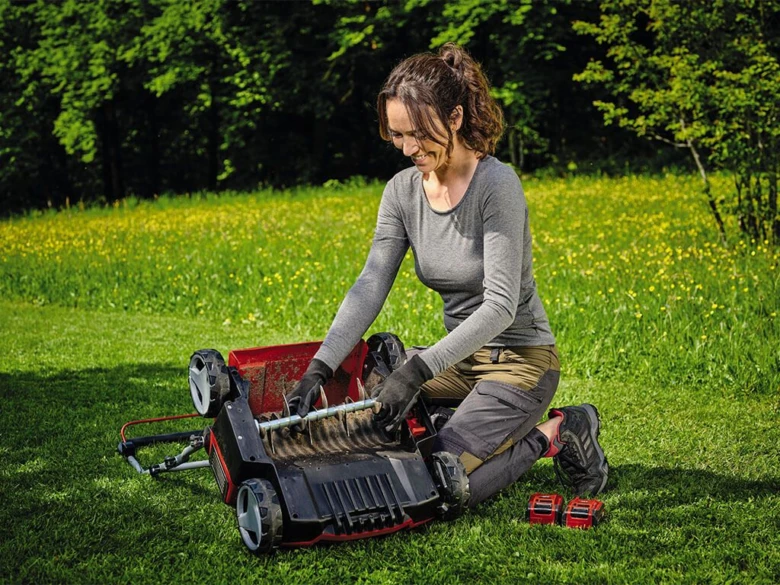 Žena provádí vertikutaci trávníku pomocí elektrického stroje.