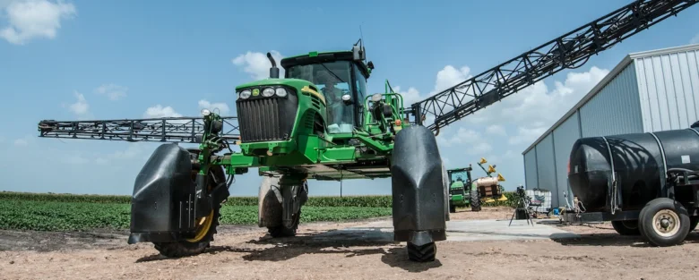 Zelený traktor pro postřik v poli bavlny.