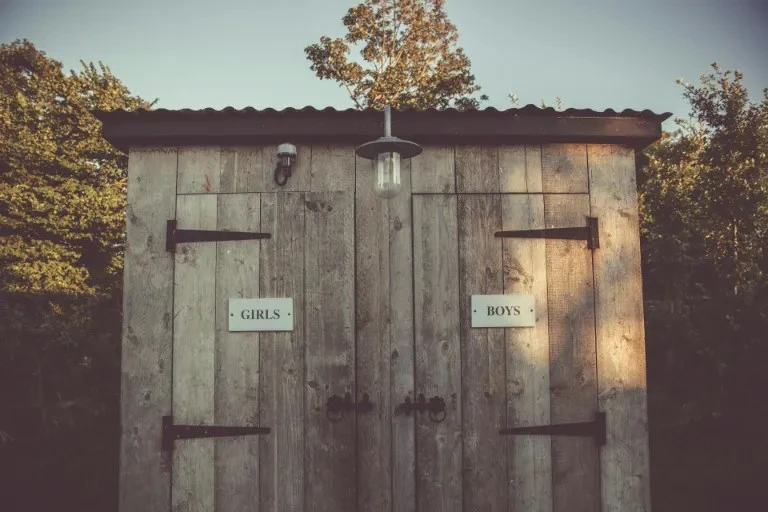Venkovní suchý záchod s dřevěnými dveřmi označenými GIRLS a BOYS.