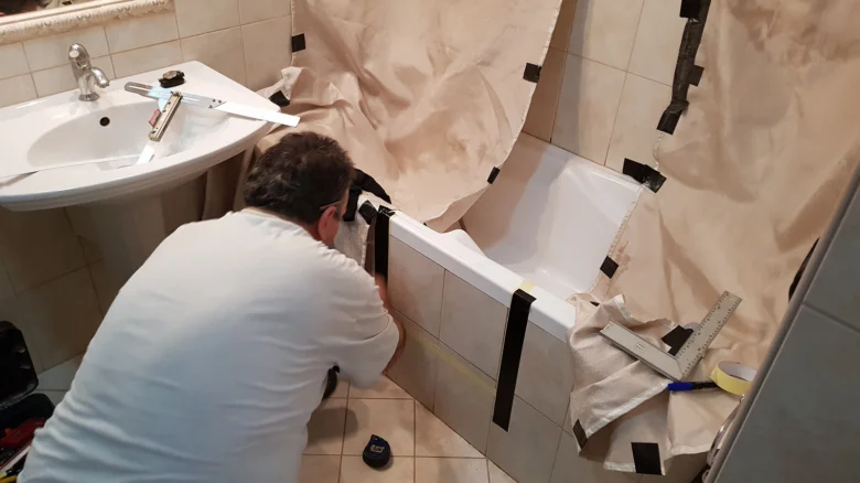 Muž instaluje dveře do vany s ochranným pláštěm.