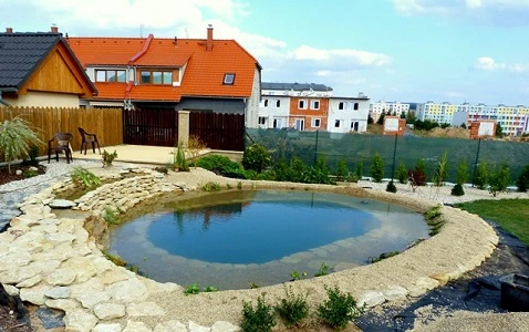 Přirozené koupací jezírko v zahradě s kamenným obvodem.