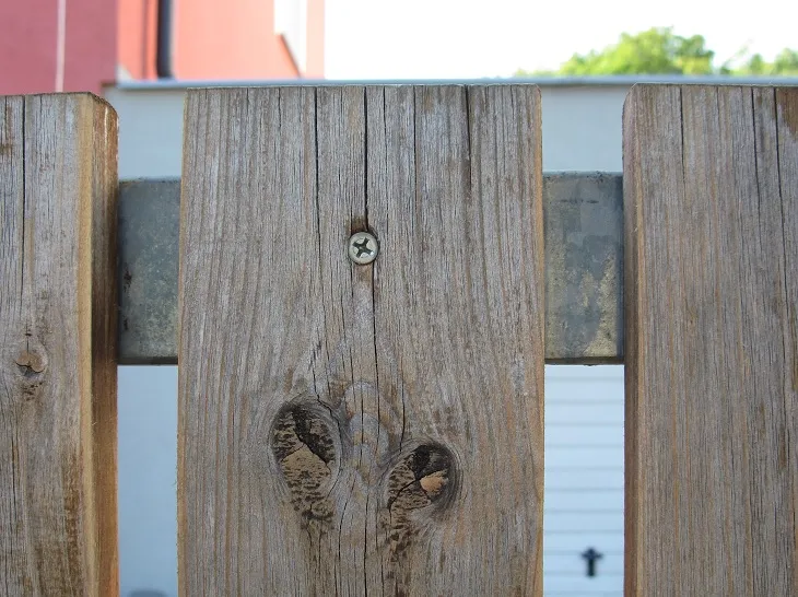 Detail dřevěného plotu s šroubem a uzly v desce.