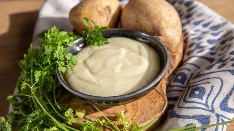 Kremová bramborová kaše s petrželkou vedle celých brambor.