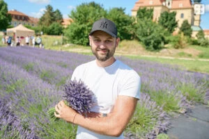 Muž drží svazek levandule v poli s kvetoucími rostlinami.