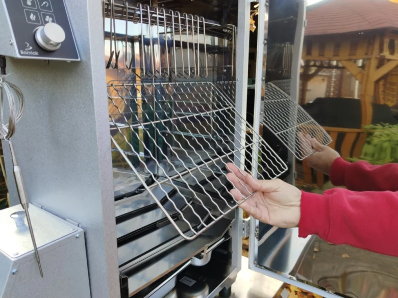 Osoba vkládá kovovou mřížku do elektrické udírny pro kouření masa.