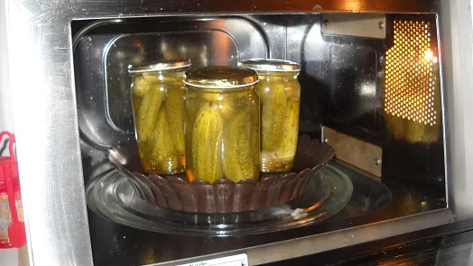 Tři sklenice s okurkami se zavařují v mikrovlnné troubě.