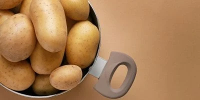 Korba s celými brambory bez slupky na hnědém pozadí.