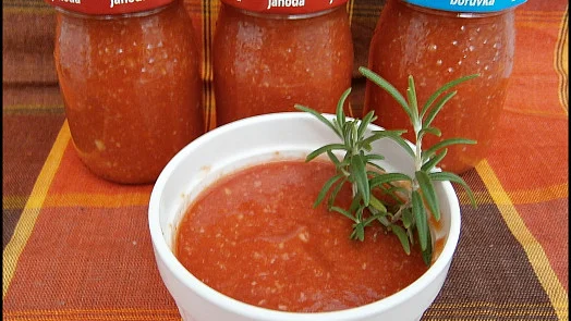 Bílá miska s rajčatovou passátou a rozmarýnem před skleničkami.