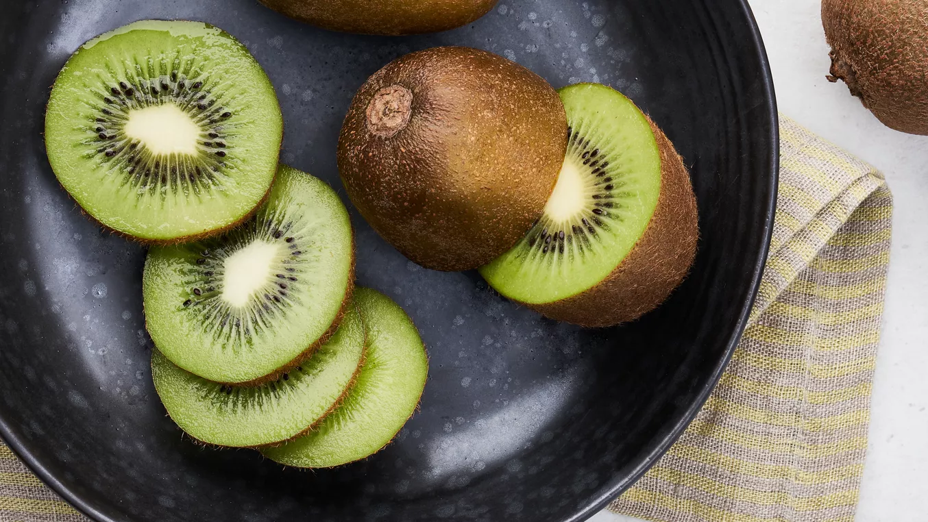 Čerstvé nakrájené zelené kiwi v černém talíři.