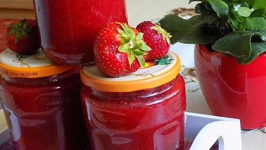 Sklenice domácí jahodové marmelády s čerstvými jahodami na víčkách.