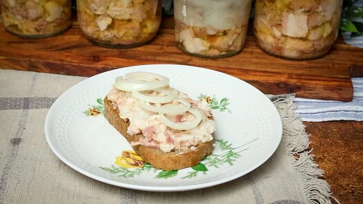 Domácí masová pasta na chlebu s cibulovými kroužky a sklenicemi zavařeného masa.