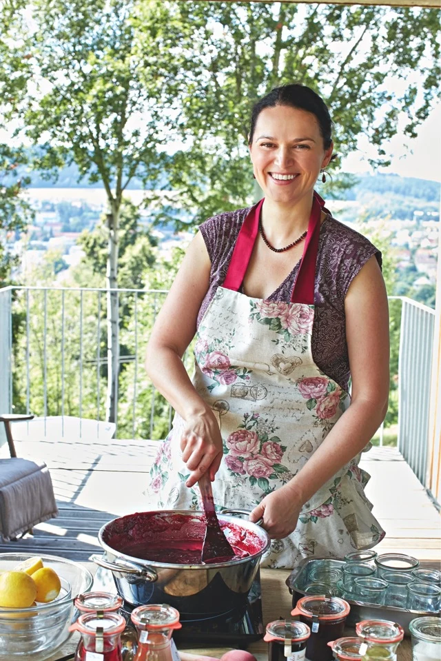Žena míchá višňovou marmeládu na venkovní terase s džemovými sklenicemi.