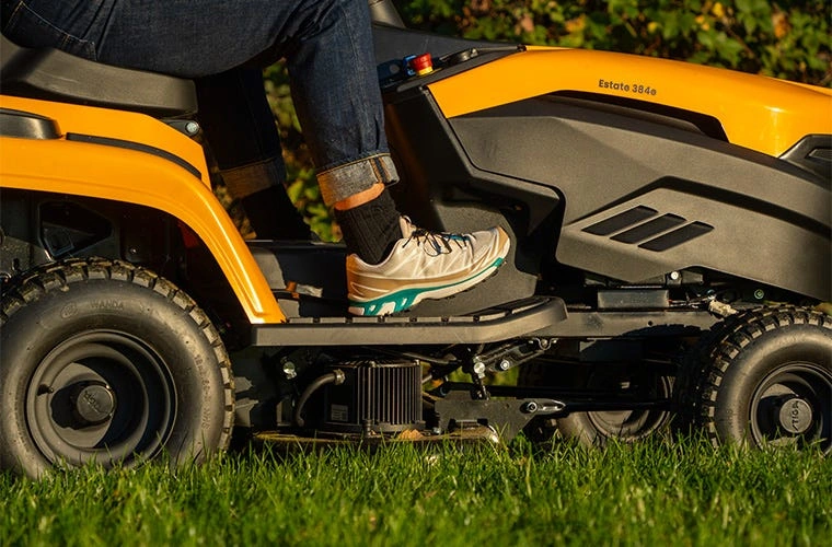 Člověk řídí žlutý traktor na trávníku pro údržbu zahrady.