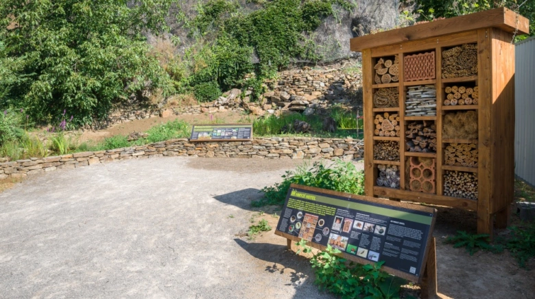 Dřevěný hmyzí hotel v zahradě s informační tabulou.