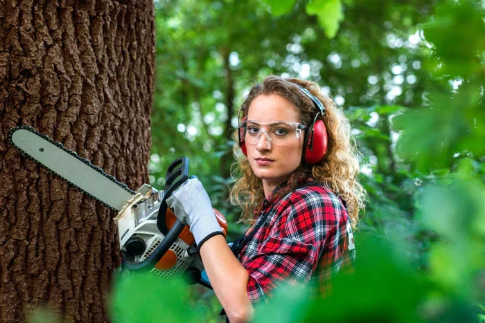 Žena s elektrickou pilou pracuje na stromě v zahradě.