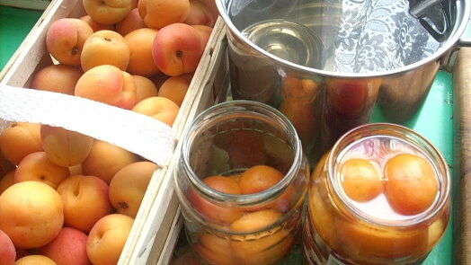 Čerstvé meruňky v krabici vedle skleniček s marmeládou.
