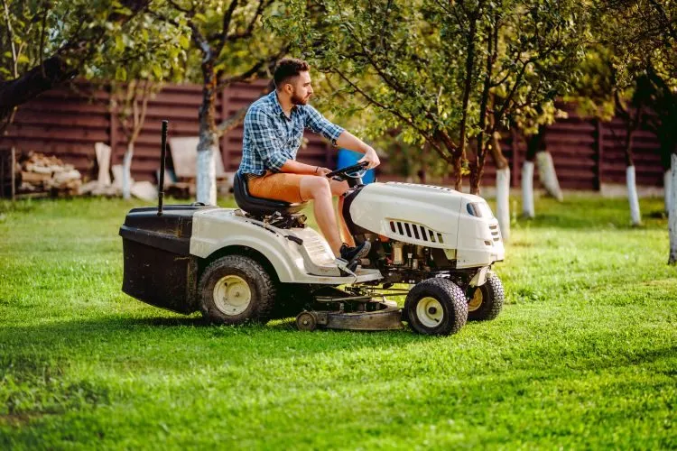 Muž řídí zahradní traktor na zelené trávníku.