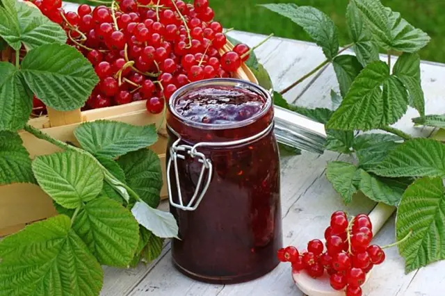 Sklenice marmelády z rybízu s čerstvými bobulemi a listy na venkovním stole.