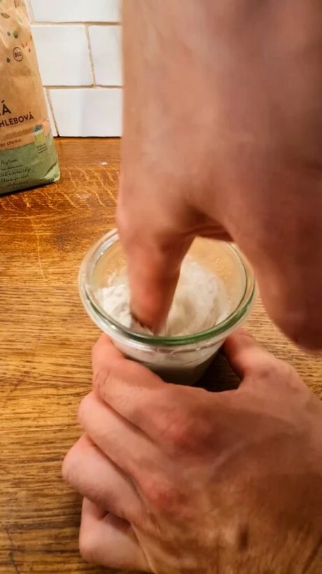 Ruka míchá kynutou těsto v malém skleněném kelímku.