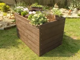 Velký dřevěný kvetinový box s rostlinami na trávníku.